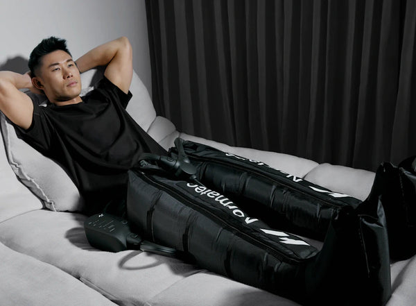 A man relaxing on a couch using the Normatec 3 Leg Recovery System | Hyperice, a recovery tool designed to improve circulation and muscle recovery through compression therapy.