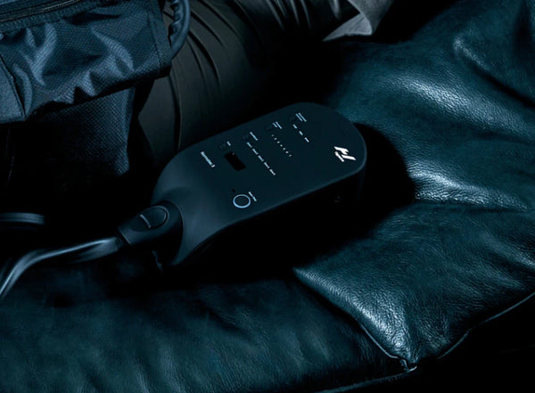 Close-up of a sleek black control unit for the Normatec 3 Leg Recovery System | Hyperice resting on a dark leather surface, highlighting its buttons and LED indicators.