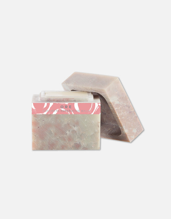 Two bars of natural soap with a soft earthy tone and a pink label, next to a clear lip balm, representing Concreta | Zents skincare products.