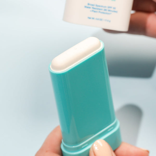 Close-up of a hand holding the Mineral Stick SPF 50 | COOLA sunscreen in a turquoise container, highlighting a smooth, solid skincare product designed for sun protection.