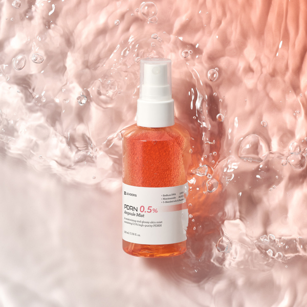 PDRN 0.5% Ampoule Mist | Leaders with orange serum droplets inside a clear spray bottle, photographed on a wet, glossy surface for skincare and hydration.