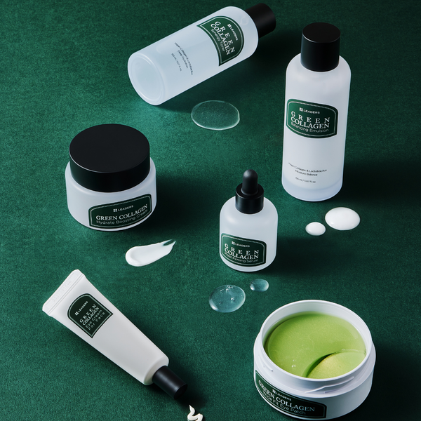 Assorted skincare products from the Green Collagen Wide Fit Eye Patch | Leaders collection displayed on a green surface, featuring jars, bottles, a dropper, and gel patches for targeted wellness and skincare.