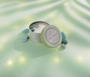 Bloom Candle Tin 6 oz | Aluminate Life with soothing stones inside on a soft green surface surrounded by natural light and shadows, evoking relaxation and wellness.