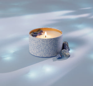 Calm Candle Tin 6 oz | Aluminate Life with a lit flame surrounded by small blue crystals on a soft blue surface, evoking a peaceful and soothing atmosphere.
