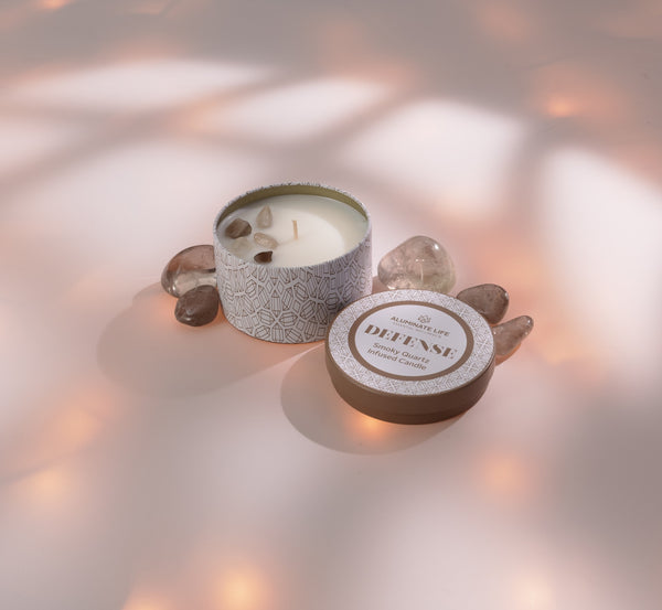 Defense Candle Tin 6 oz | Aluminate Life with a decorative patterned tin, topped with small crystals, surrounded by smooth stones on a soft, warm-toned surface.
