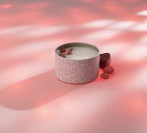 Energy Candle Tin 6 oz | Aluminate Life with decorative pink patterned container, small stones beside it on soft pink surface with gentle lighting, evoking relaxation and wellness.