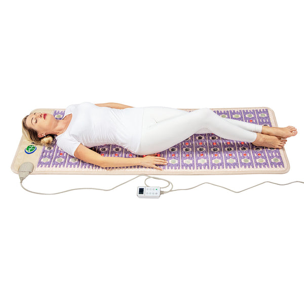 Woman lying on a purple and beige therapeutic wellness mat with a control device, demonstrating relaxation using the TAJ-Mat™ Full 7224 Firm - Photon PEMF InfraMat Pro® | HealthyLine.