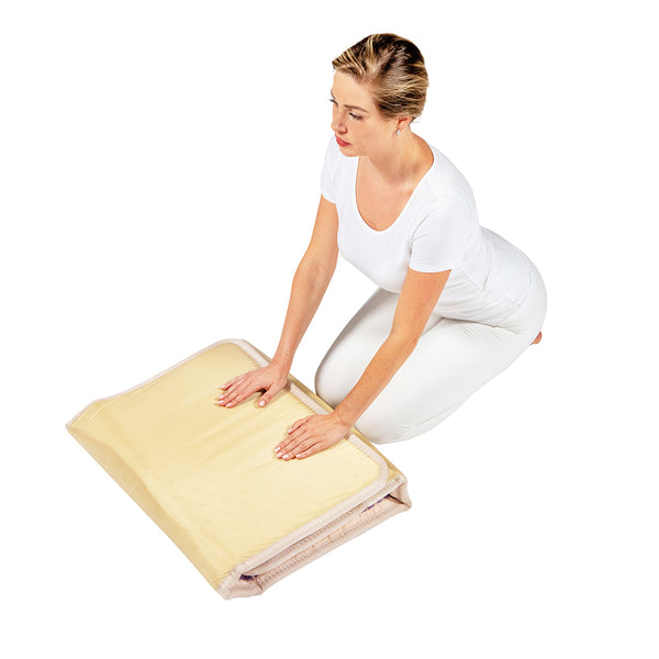 A woman in white attire kneeling and unfolding the TAJ-Mat™ Full Short 6024 Firm - Photon PEMF InfraMat Pro® | HealthyLine wellness device on a white background.
