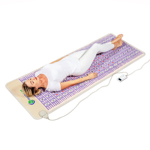 Woman lying relaxed on a purple wellness device mat with embedded stones connected to a remote control, demonstrating the TAJ-Mat™ Large 8030 Firm - Photon PEMF (Right/Standard) Inframat Pro® | HealthyLine for body care and recovery.