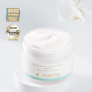 Open jar of Nourishing Body Butter | Pure Fiji with creamy white texture, displayed on a white surface with a white flower in the background and award badges visible nearby.