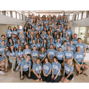 Large diverse group of people wearing matching blue Wellness Varsity T-Shirt | Lucky Owl, gathered indoors smiling and posing together for a group photo.