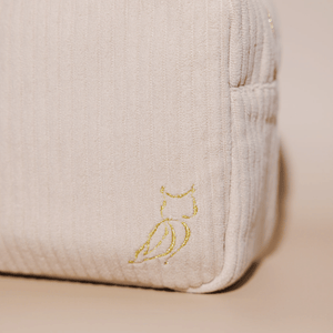 Close-up of a beige textured Luxe Travel Bag | Lucky Owl corner with a subtle gold embroidered owl logo, highlighting the bag’s refined and elegant design.