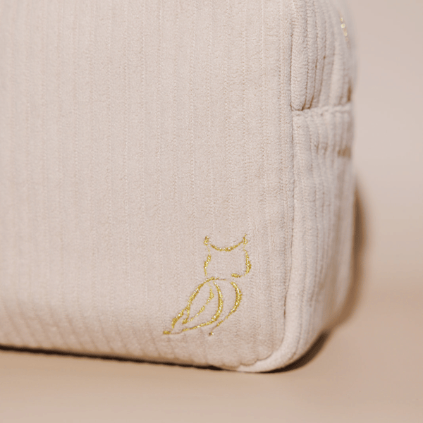 Close-up of a beige textured Luxe Travel Bag | Lucky Owl corner with a subtle gold embroidered owl logo, highlighting the bag’s refined and elegant design.
