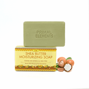 Green bar soap embossed with "PRIMAL ELEMENTS" resting on a yellow box labeled Shea Butter Moisturizing Soap alongside shea nuts, showcasing Luxury Shea Butter Moisturizing Soap | Primal Elements for skincare and body care.