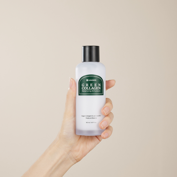 Hand holding a frosted bottle of Green Collagen Balancing Emulsion | Leaders skincare product with a black cap against a neutral background.