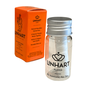 Clear glass jar with metal lid containing white dental floss beside bright orange packaging box for Microfiber Floss | LINHART designed for oral health and reuse.
