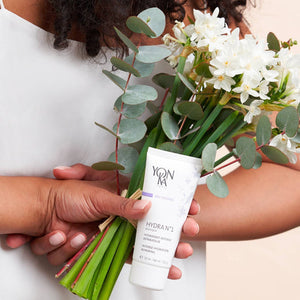 Person holding a bouquet of white flowers and eucalyptus leaves while displaying a tube of Hydra No. 1 Masque Sleep Gel Mask | Yon-Ka Paris skincare product.