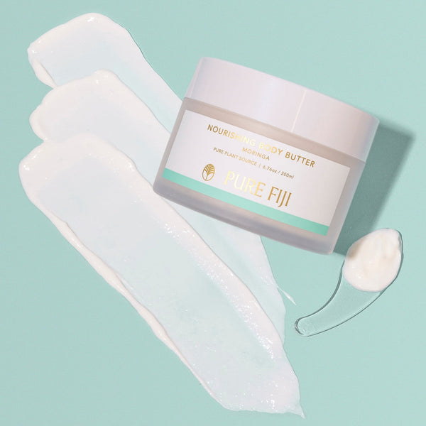 Jar of Nourishing Body Butter | Pure Fiji with smooth creamy white body butter spread on pastel green surface alongside a small dollop on a clear spoon, highlighting rich moisturizing texture for skincare and body care.