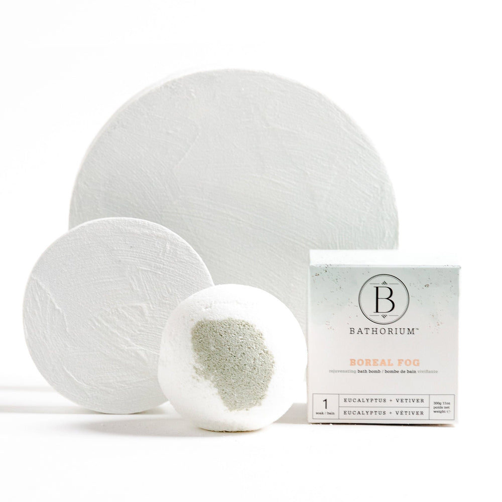 Boreal Fog Bath Bomb | Bathorium featuring a white bath bomb with gray powder and eucalyptus plus vetiver scent, packaged in a minimalist white box promoting skincare and wellness.