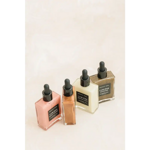 Four glass dropper bottles containing different tinted skincare oils, featuring the Bronzée Shimmer Oil| French Girl for body care and a radiant shimmer effect.