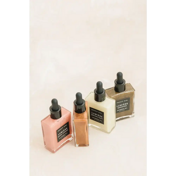 Four glass dropper bottles containing different tinted skincare oils, featuring the Bronzée Shimmer Oil| French Girl for body care and a radiant shimmer effect.