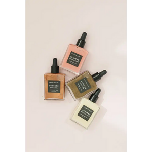Four glass bottles of Bronzée Shimmer Oil| French Girl in various shades including pink, gold, bronze, and cream, each with black dropper caps on a light background, showcasing skincare body care products.