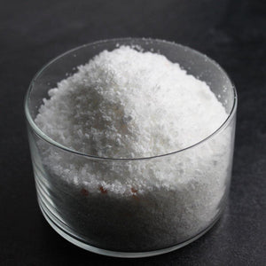 Clear glass container filled with white crystalline Tahitian Vanilla Bubbling Bath Salts | Primal Elements, displayed on a dark surface for skincare and wellness use.