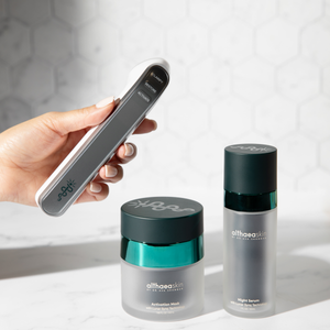 Hand holding a sleek wellness device next to Althaea Skin Activation Mask and Night Serum jars, all part of the C·A·R·A Multi-Modal Tool Kit | Althaea Skin skincare collection.