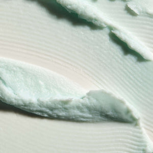 Close-up texture of a smooth, creamy, light mint green Cleansing Foam | Omorovicza skincare product spread on a white surface.