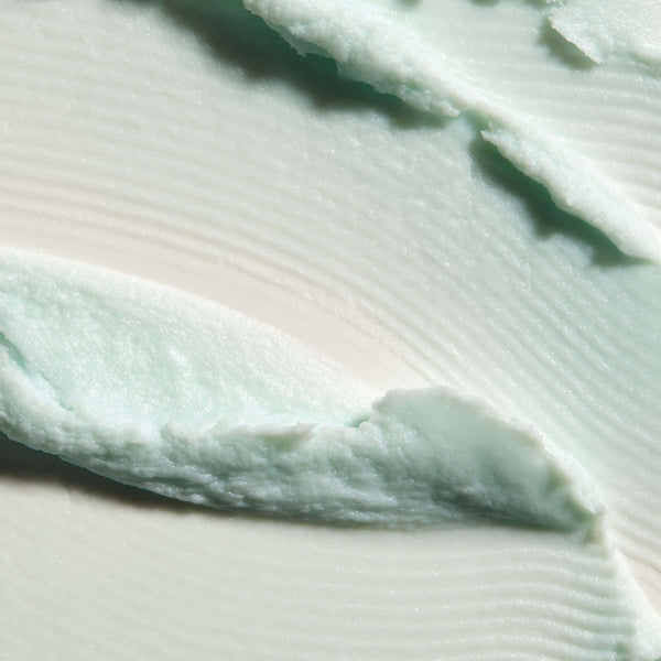 Close-up texture of a smooth, creamy, light mint green Cleansing Foam | Omorovicza skincare product spread on a white surface.