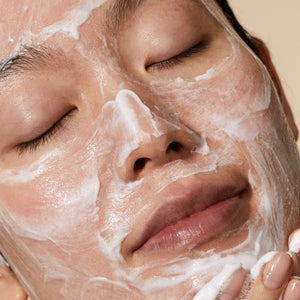 Close-up of a person with eyes closed gently applying Cleansing Foam | Omorovicza skincare product on their face, showcasing a smooth, creamy texture for a soothing skincare routine.