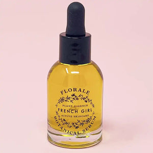 Clear glass dropper bottle filled with golden liquid labeled Florale Botanical Serum | French Girl, a skincare product set against a soft pink background.