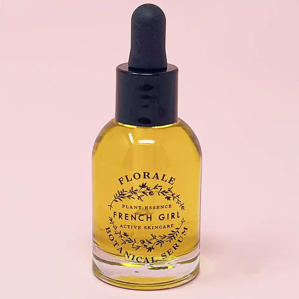 Clear glass dropper bottle filled with golden liquid labeled Florale Botanical Serum | French Girl, a skincare product set against a soft pink background.