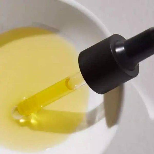 Close-up of a dropper dispensing yellow liquid into a white dish, showcasing the Florale Botanical Serum | French Girl for skincare and wellness routines.