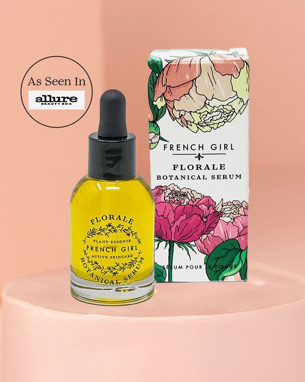 Glass dropper bottle of Florale Botanical Serum | French Girl with yellow liquid next to white floral-illustrated packaging on a pink surface and background with Allure magazine feature badge.