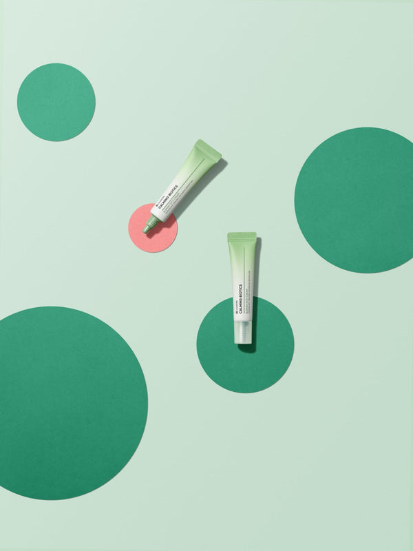 Two tubes of Calming Biotics Blemish Spot Cream | Leaders on a light green background with green and pink circular shapes, highlighting skincare and wellness themes.