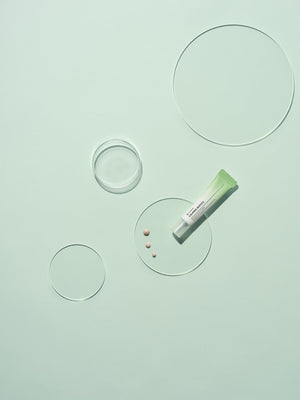 Tube of Calming Biotics Blemish Spot Cream | Leaders on a pale green surface with clear round glass plates and small cream dots, showcasing the skincare product for targeted blemish care.