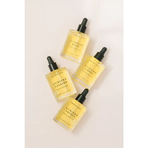 Four glass dropper bottles of skincare oils labeled with different fragrances, featuring Lumière Body Glow Oil - Rose | French Girl, arranged on a light surface for body care and wellness.