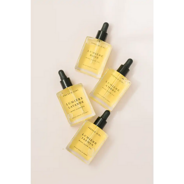 Four glass dropper bottles of skincare oils labeled with different fragrances, featuring Lumière Body Glow Oil - Rose | French Girl, arranged on a light surface for body care and wellness.