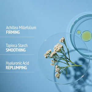 Close-up of natural skincare ingredients including Achillea Millefolium flowers in a glass dish with drops of liquid, highlighting firming, smoothing, and replumping benefits for Sublime Lift-Mask | [ comfort zone ].