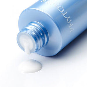 Close-up of a blue bottle dispensing white cleansing milk lotion onto a white surface, featuring Perfect Visage Gentle Cleansing Milk | Phytomer skincare product.