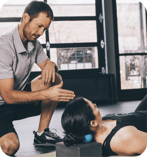 A man guides a woman using the RAD Roller Original | RAD under her neck for targeted muscle recovery and relief in a wellness setting.
