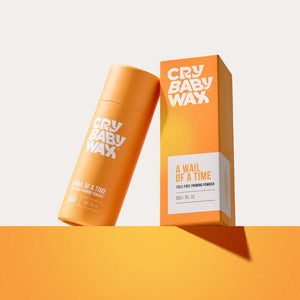 Orange cylindrical container and matching box of A Wail of a Time Priming Powder | Crybaby Wax displayed on an orange surface with light shadow, promoting skincare product.