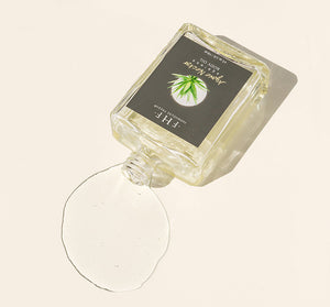 Agave Nectar Ageless Body Oil | Farmhouse Fresh bottle tilted with clear oil spilling on a light surface, showcasing a fresh natural skincare product for body care and wellness.