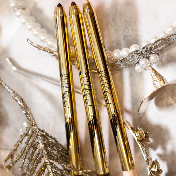 Three gold Writing on the Wall Eyeliner Pencil | Pretty Vulgar products displayed with pearl and glittery decorative accessories on a soft surface.