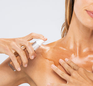 Close-up of a woman applying Lustre Drench® Instant Glow Dry Oil | Farmhouse Fresh to her shoulder, highlighting glowing, moisturized skin in a skincare routine.