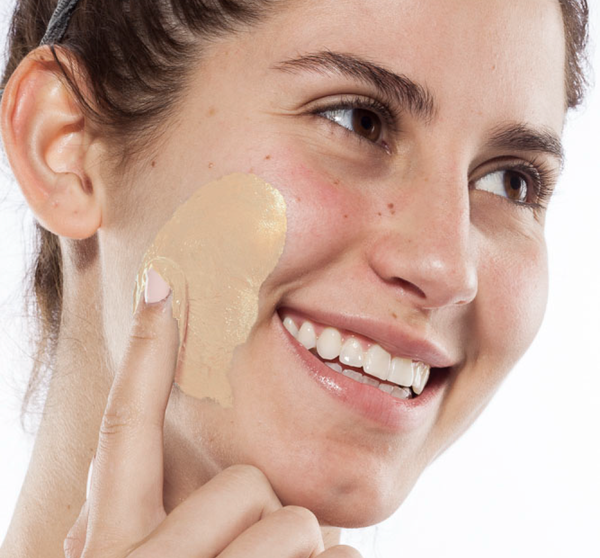 Woman smiling as she applies a creamy face mask to her cheek, demonstrating skincare with the Fast Fix Face Mask Sampler | Farmhouse Fresh for a glowing complexion.