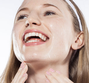 A woman with clear skin and a white headband gently applying Green Tea Milk Wash | Farmhouse Fresh to her face, smiling and enjoying her skincare routine.