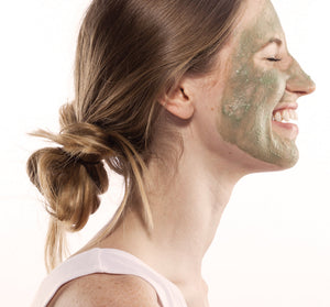 Smiling woman with a green facial mask applied, enjoying a moment of skincare relaxation using Hydration Cascade® 3-step Instant Spa Facial | Farmhouse Fresh.