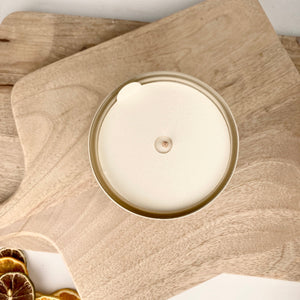 Top view of an unlit Santal + Coconut 10 oz Candle | ROAM Homegrown with a wooden wick, placed on a light wooden cutting board next to dried citrus slices.